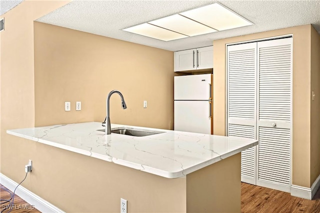 kitchen with light stone countertops, wood finished floors, a sink, freestanding refrigerator, and a peninsula