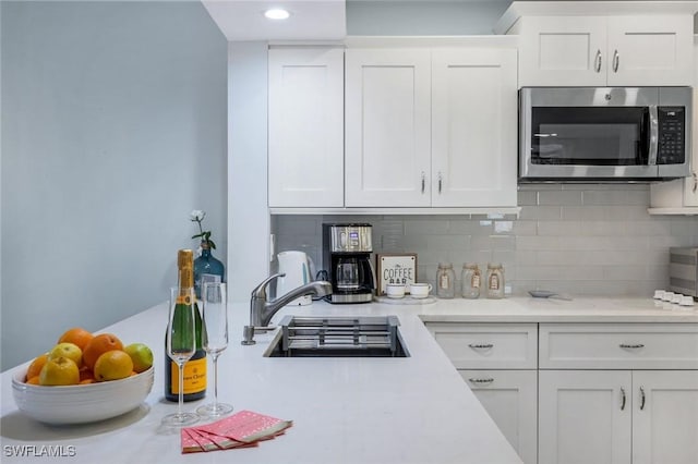 kitchen with light countertops, stainless steel microwave, decorative backsplash, and white cabinets