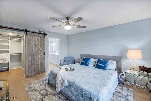 bedroom with a walk in closet, visible vents, a barn door, and wood finished floors