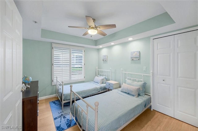 bedroom with a closet, baseboards, light wood-type flooring, a tray ceiling, and a ceiling fan