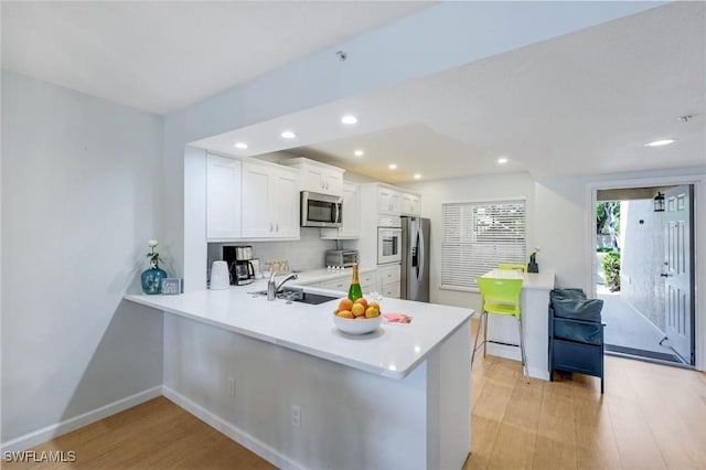 kitchen with appliances with stainless steel finishes, a sink, light wood-style floors, light countertops, and baseboards