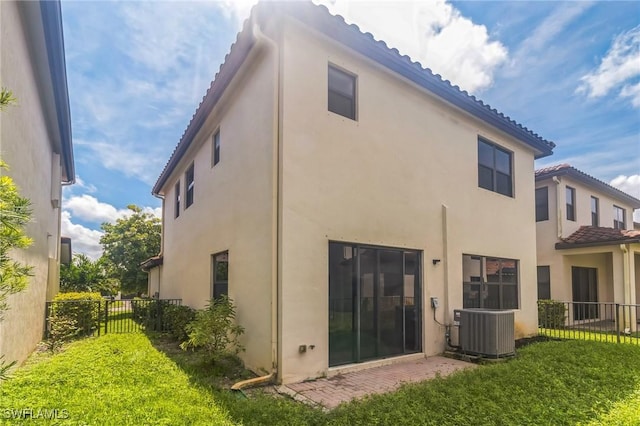 rear view of house featuring central air condition unit, stucco siding, a lawn, fence, and a tile roof