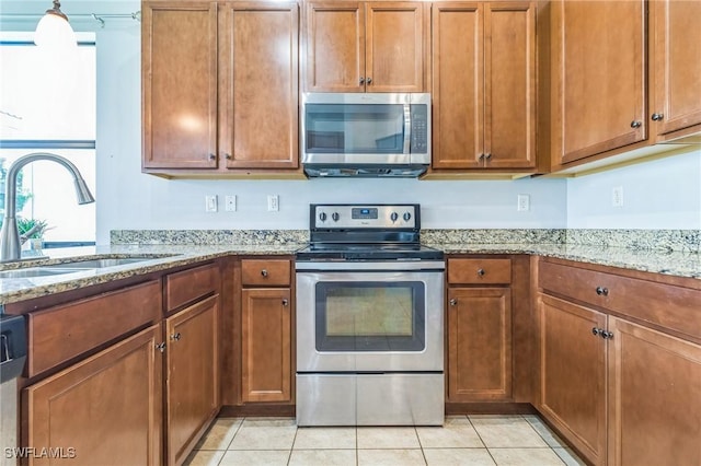 kitchen with stainless steel appliances, brown cabinets, a sink, and light tile patterned flooring