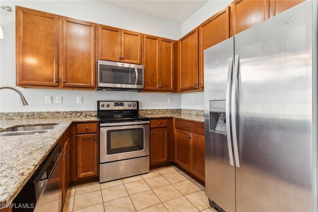 kitchen with light tile patterned floors, light stone countertops, brown cabinetry, appliances with stainless steel finishes, and a sink