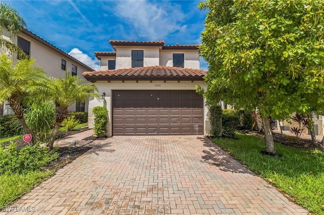 mediterranean / spanish house with a garage, stucco siding, a tiled roof, and decorative driveway