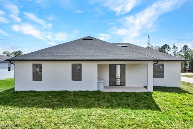 rear view of house featuring a shingled roof, a lawn, and stucco siding