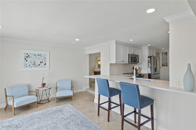 kitchen featuring crown molding, light countertops, a breakfast bar area, stainless steel appliances, and decorative backsplash