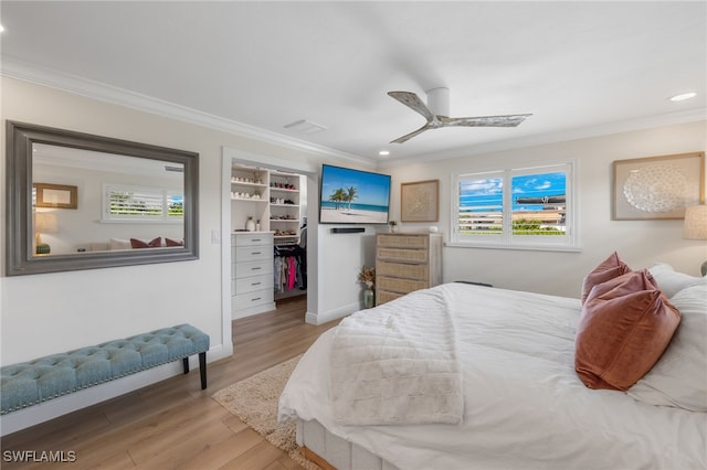 bedroom featuring light wood finished floors, a walk in closet, ornamental molding, and a ceiling fan