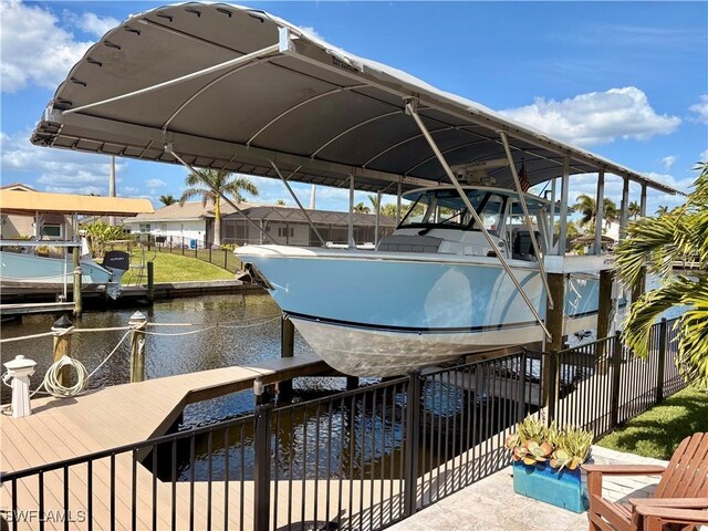 dock area with boat lift, a water view, and fence