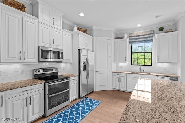 8756 Bellano Ct Unit 201, Naples, FL 34119 - kitchen with appliances with stainless steel finishes, a sink, crown molding, white cabinetry, and light wood-type flooring