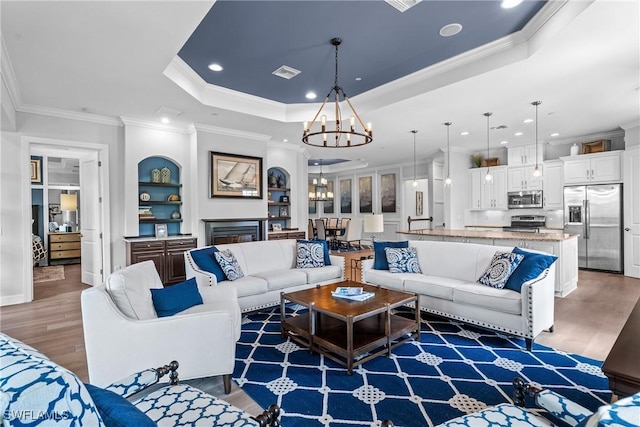living area featuring recessed lighting, wood finished floors, ornamental molding, a notable chandelier, and a tray ceiling
