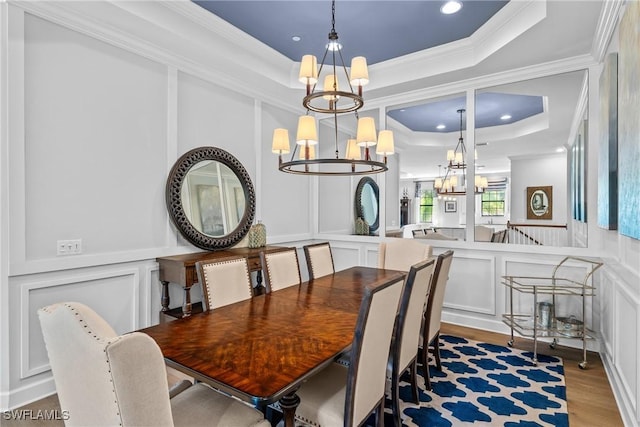 dining space featuring wood finished floors, an inviting chandelier, a decorative wall, ornamental molding, and a raised ceiling