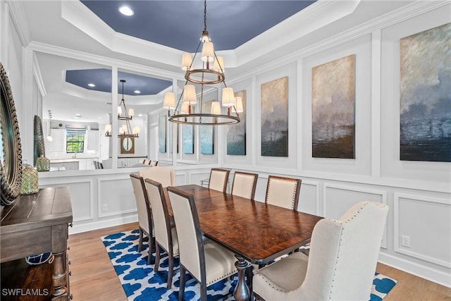dining area with an inviting chandelier, a decorative wall, light wood-style floors, ornamental molding, and a tray ceiling