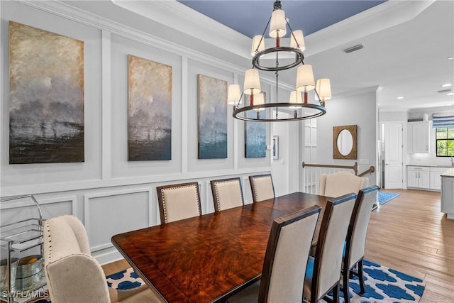 dining area featuring crown molding, a decorative wall, and light wood-style floors
