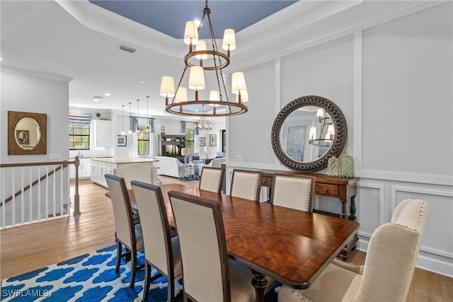 dining space featuring crown molding, visible vents, a chandelier, a tray ceiling, and light wood finished floors
