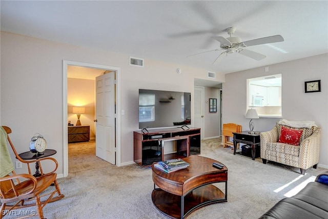 living area featuring baseboards, visible vents, a ceiling fan, and light colored carpet