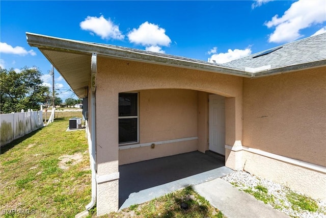 entrance to property featuring central AC unit, stucco siding, fence, and a yard