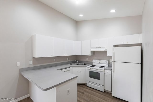 kitchen with a peninsula, white appliances, under cabinet range hood, white cabinetry, and a sink