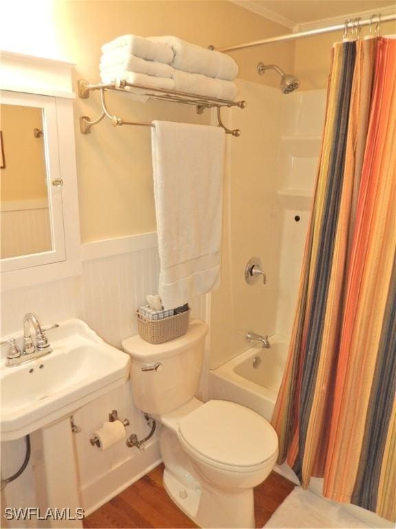 full bath featuring wood finished floors, toilet, shower / bathtub combination with curtain, a wainscoted wall, and a sink