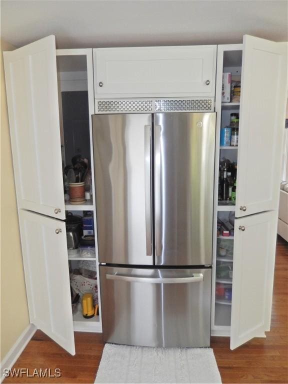 kitchen with freestanding refrigerator, white cabinetry, wood finished floors, and glass insert cabinets