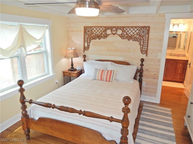 bedroom with a sink, wood walls, baseboards, wood finished floors, and ensuite bathroom