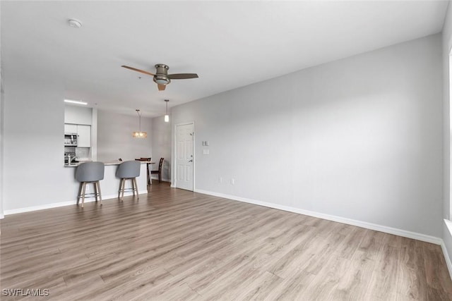 living area featuring light wood finished floors, baseboards, and ceiling fan