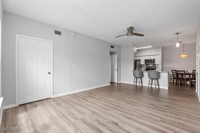 unfurnished living room with baseboards, ceiling fan, visible vents, and light wood-style floors