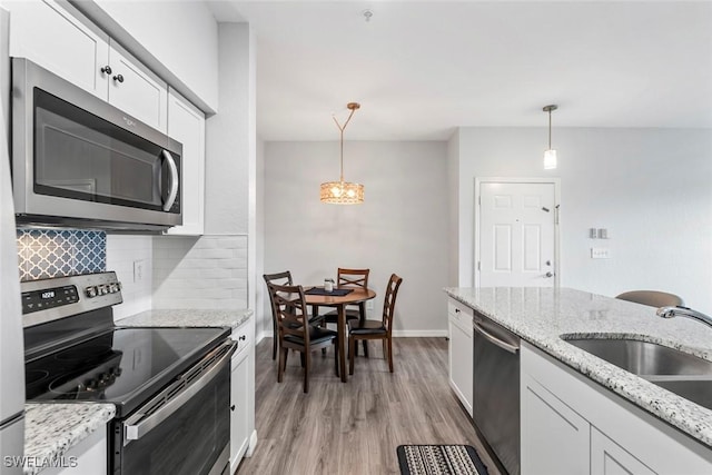 kitchen with white cabinetry, decorative light fixtures, stainless steel appliances, backsplash, and light wood-style flooring