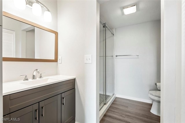 full bathroom with toilet, vanity, a shower stall, wood finished floors, and baseboards
