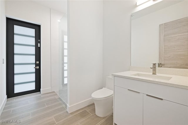 309 SW 15th Ter, Cape Coral, FL 33991 - bathroom featuring vanity, toilet, baseboards, walk in shower, and wood tiled floor
