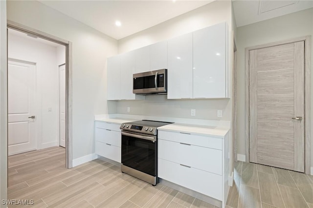 309 SW 15th Ter, Cape Coral, FL 33991 - kitchen featuring white cabinetry, light countertops, wood finish floors, modern cabinets, and appliances with stainless steel finishes