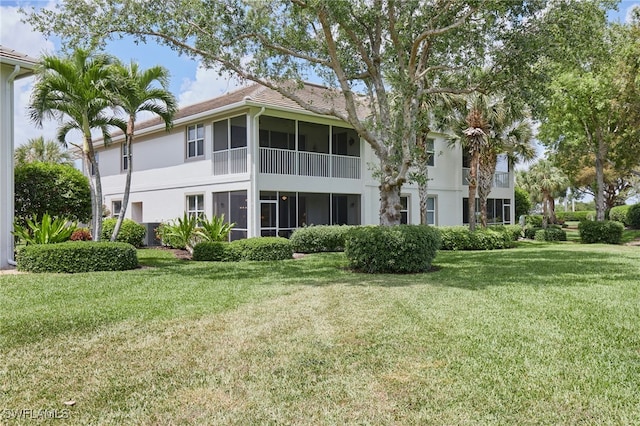 rear view of house with a yard, stucco siding, and a sunroom