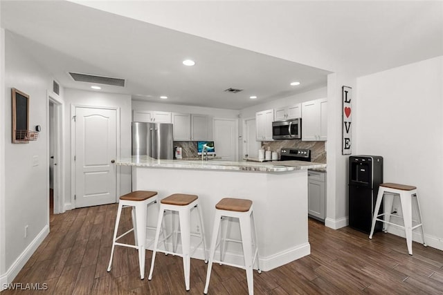 3009 35th St SW, Lehigh Acres, FL 33976 - kitchen featuring a breakfast bar area, backsplash, visible vents, appliances with stainless steel finishes, and dark wood-style floors