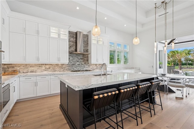 3359 Fanny Bay Ln N, Naples, FL 34114 - kitchen featuring wall chimney range hood, light wood-style floors, decorative backsplash, an island with sink, and recessed lighting