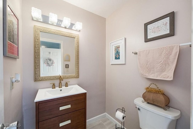 half bathroom with vanity, baseboards, and toilet
