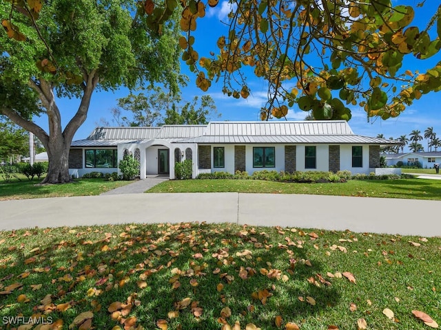 ranch-style house with a standing seam roof, a front yard, metal roof, and stone siding