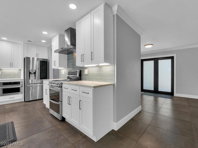 kitchen with crown molding, light countertops, wall chimney exhaust hood, backsplash, and stainless steel appliances