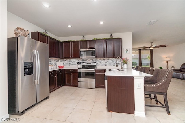 kitchen featuring appliances with stainless steel finishes, a peninsula, a sink, open floor plan, and a breakfast bar