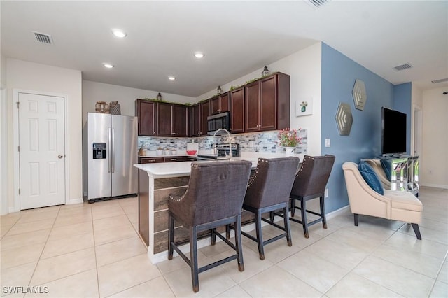 kitchen with stainless steel appliances, light countertops, dark brown cabinets, a peninsula, and backsplash