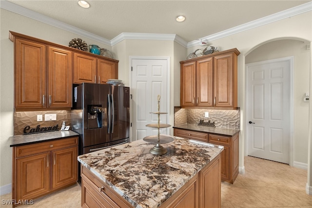 kitchen with arched walkways, ornamental molding, stainless steel refrigerator with ice dispenser, dark stone countertops, and brown cabinets