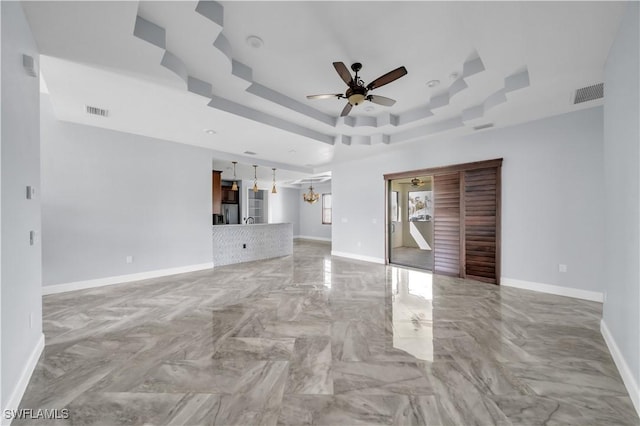 unfurnished living room featuring visible vents, a ceiling fan, a tray ceiling, and baseboards