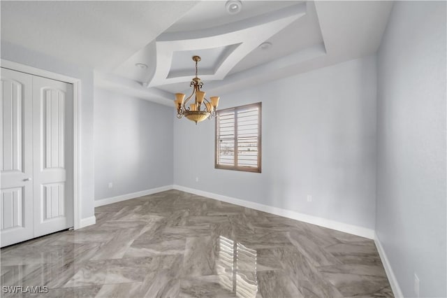 unfurnished bedroom featuring a closet, a tray ceiling, a chandelier, and baseboards