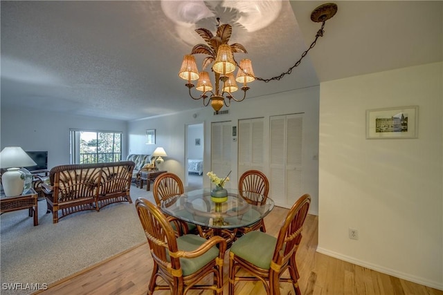 dining area with baseboards, light wood-type flooring, a notable chandelier, and a textured ceiling