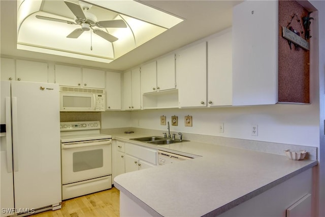 kitchen featuring a raised ceiling, a sink, light countertops, white appliances, and light wood finished floors