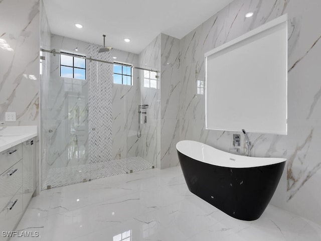 bathroom with a freestanding bath, tile walls, stone wall, vanity, and a marble finish shower