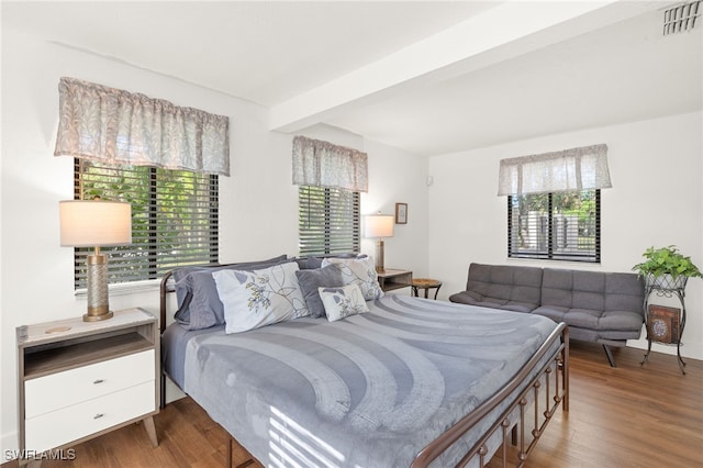 bedroom featuring multiple windows, beam ceiling, visible vents, and wood finished floors