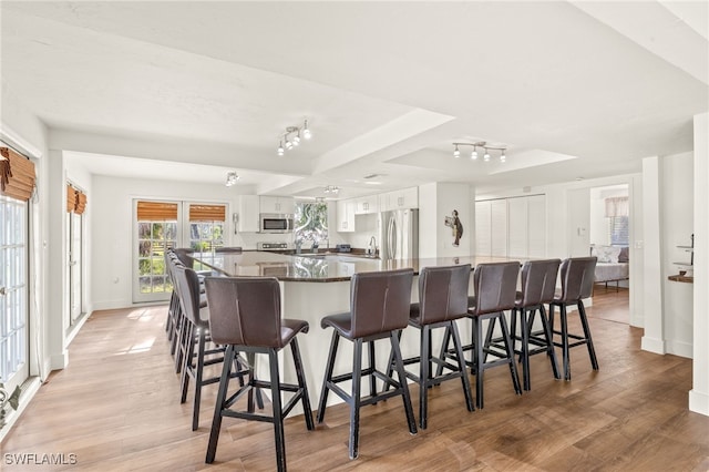 kitchen featuring appliances with stainless steel finishes, white cabinetry, a raised ceiling, light wood-style floors, and a spacious island