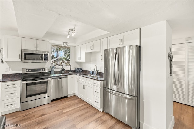 kitchen with white cabinets, light wood-style floors, stainless steel appliances, and a raised ceiling
