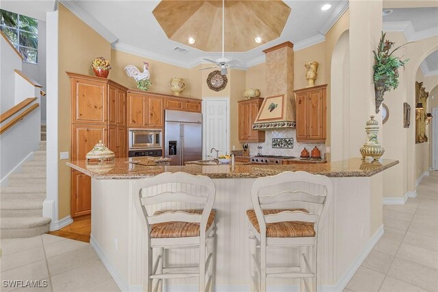kitchen with light stone countertops, arched walkways, custom range hood, built in appliances, and backsplash