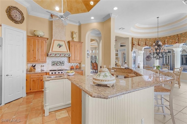 kitchen featuring a raised ceiling, arched walkways, a sink, an island with sink, and ceiling fan with notable chandelier